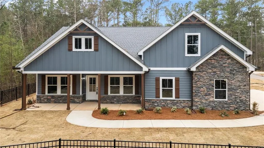 Craftsman house with a fenced front yard, a porch, stone siding, board and batten siding, and a shingled roof