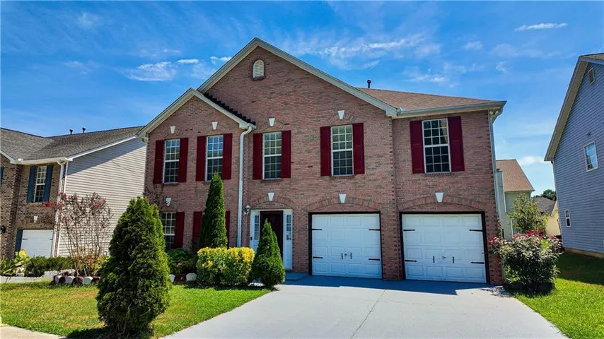 Brick Colonial two-story residence featuring a symmetrical facade with red shutters, multiple windows with white trim, and a two-car garage with blue doors