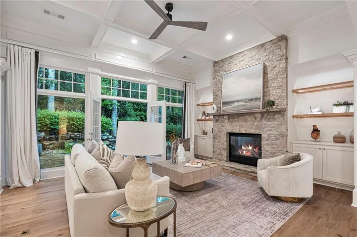 Living area featuring a stone-clad fireplace with a hearth, coffered ceiling, new hardwood flooring, and expansive windows that open to the koi pond with waterfalls.