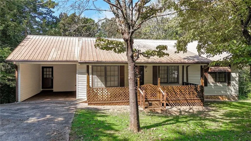 White siding exterior with a brown metal roof, featuring a covered porch with wood lattice railing, a paved driveway, and a covered carport