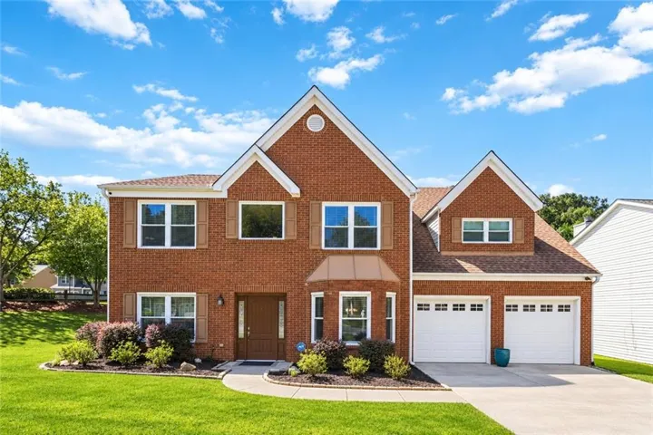 Red brick exterior with white trim, a gabled roofline, a two-car garage, and a manicured lawn