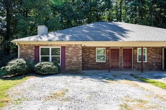 Brick exterior featuring red shutters, a shingled roof, a chimney, and a gravel front area