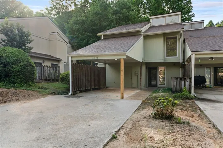 Exterior featuring a covered carport, pitched roof, multiple windows, and a partially fenced side yard