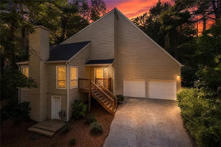 Multi-level exterior with neutral-toned siding, a two-car garage, and a prominent wood staircase leading to the main entrance