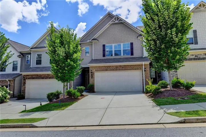 Multi-story residence featuring a two-car garage, brick and siding exterior, mature tree, and concrete driveway