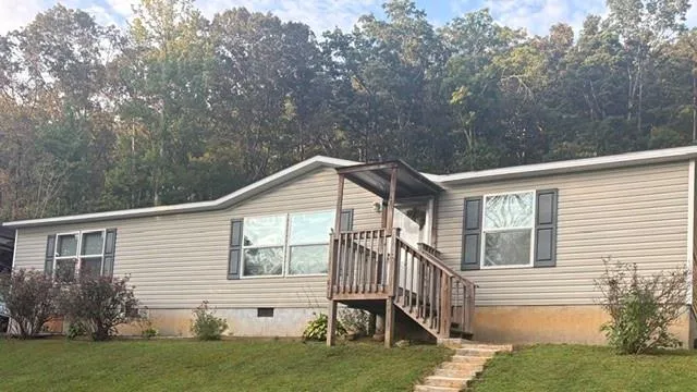 Siding exterior with contrasting dark window shutters, framed by mature trees