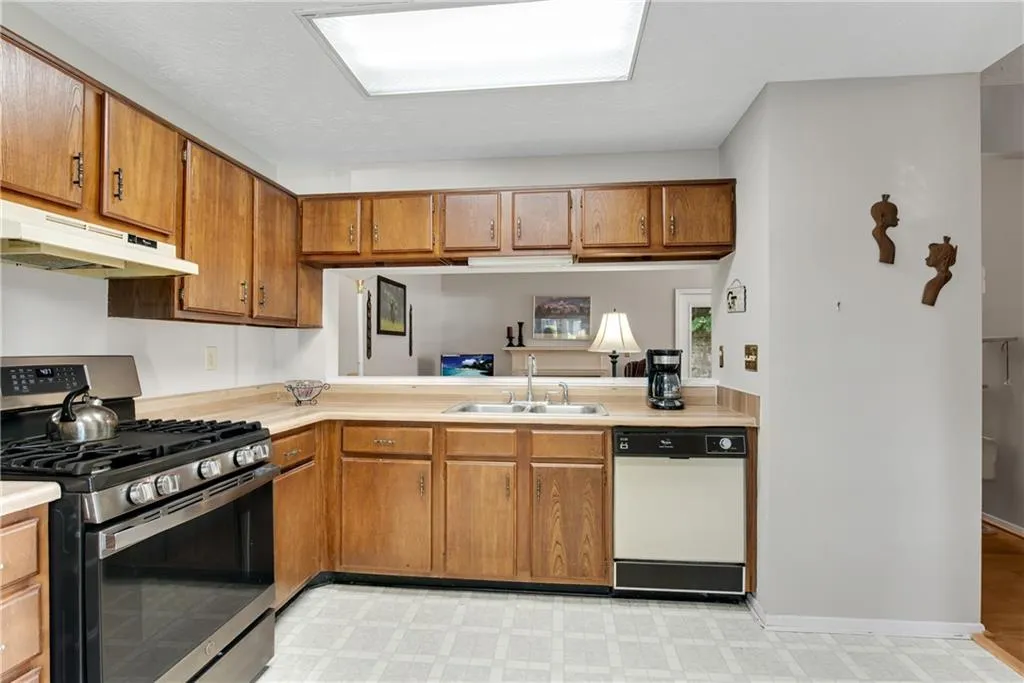Kitchen featuring light tile patterned floors, kitchen peninsula, stainless steel range with gas cooktop, white dishwasher, and sink Kitchen featuring light tile patterned floors, kitchen peninsula, stainless steel range with gas cooktop, white dishwasher, and sink