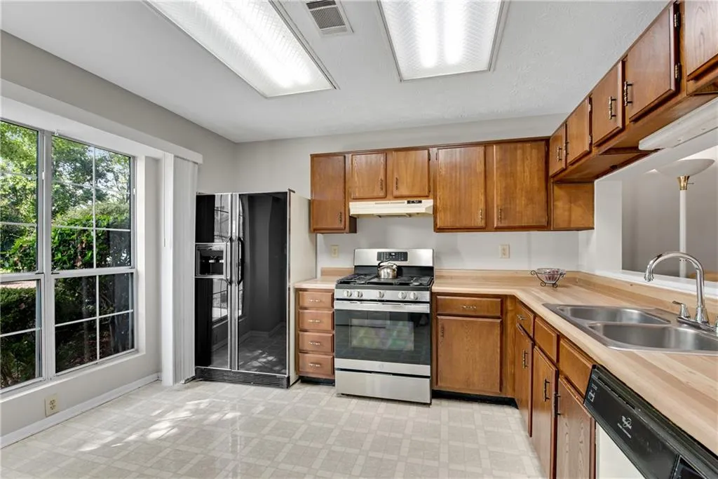 Kitchen featuring sink, stainless steel gas range oven, light tile patterned flooring, dishwasher, and black refrigerator with ice dispenser Kitchen featuring sink, stainless steel gas range oven, light tile patterned flooring, dishwasher, and black refrigerator with ice dispenser