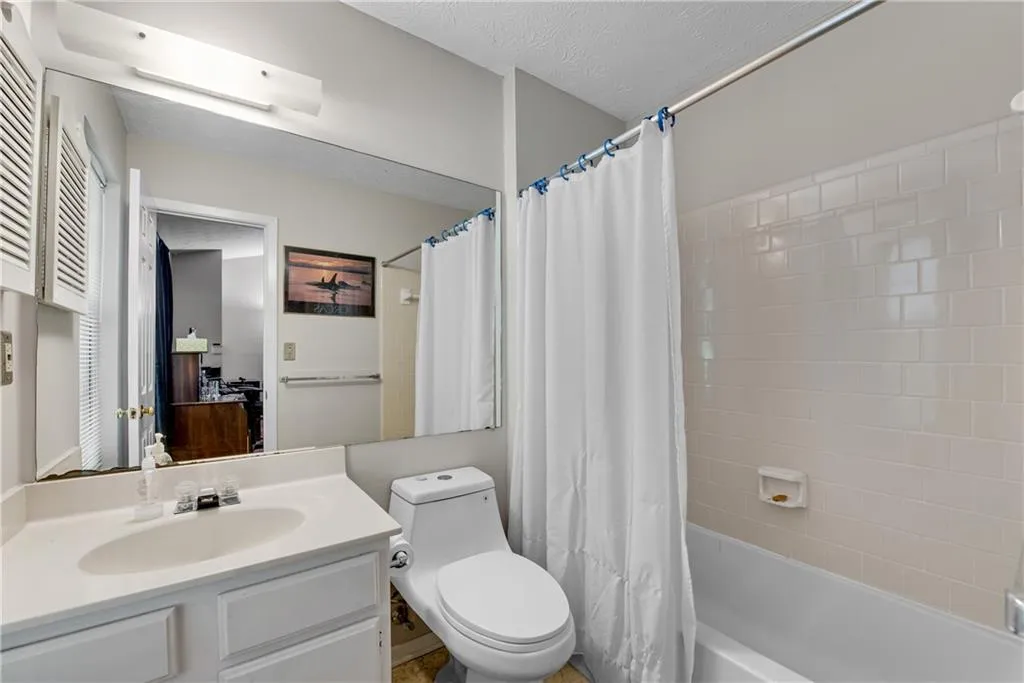 Full bathroom featuring vanity, shower / bath combo with shower curtain, a textured ceiling, and toilet Full bathroom featuring vanity, shower / bath combo with shower curtain, a textured ceiling, and toilet