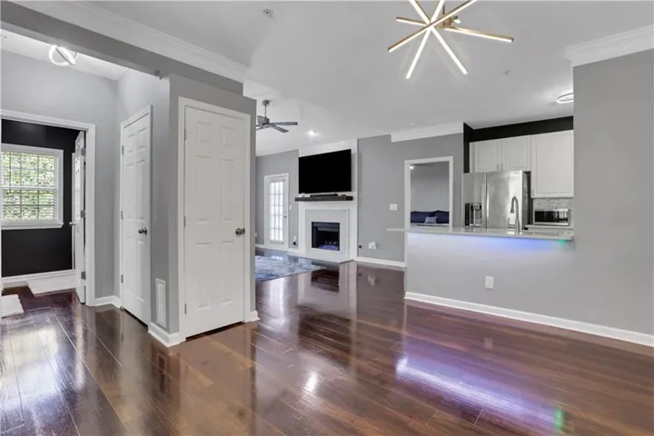 Open-concept living space featuring wood-finish flooring, a contemporary linear chandelier, and a kitchen pass-through with a light-colored countertop