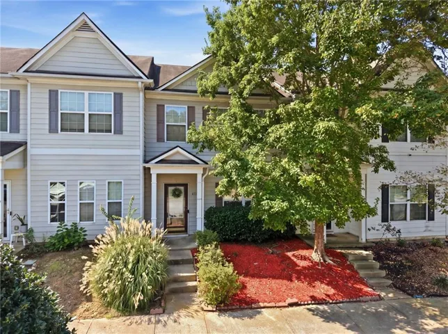 Two-story townhouse exterior with light-colored siding, dark shutters, and a covered entry