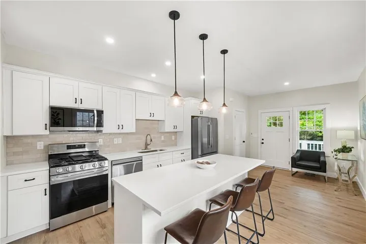 Modern kitchen with white cabinetry, stainless steel appliances, a center island with pendant lighting, and wood-finish flooring