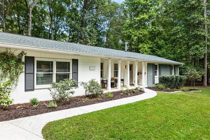 White exterior with dark shutters, covered front entry with columns, well-maintained lawn, and mature trees