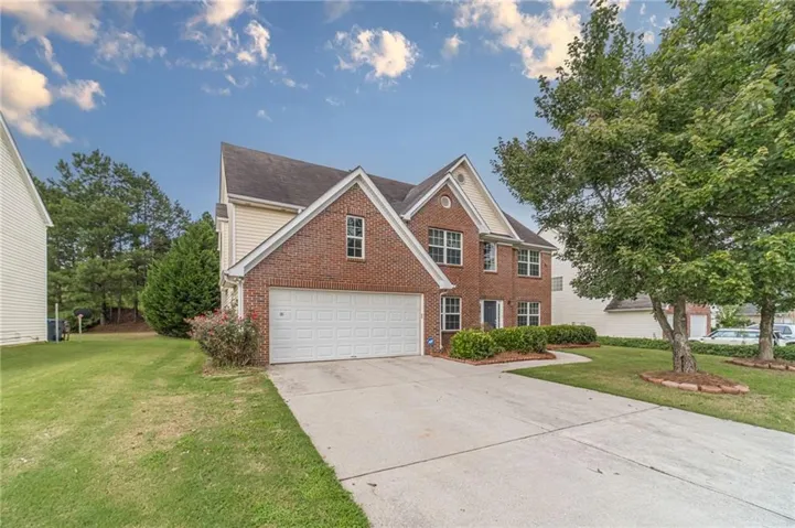 Charming two-story brick Colonial with a welcoming front elevation, featuring a white garage door, peaked roofline with dormers, and a concrete driveway