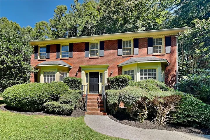 Brick exterior with a manicured front lawn, mature landscaping, and an inviting entry