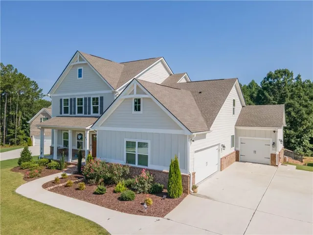 Light-toned exterior siding with brick accents, prominent gabled rooflines, covered front porch, attached garage, and mature landscaping