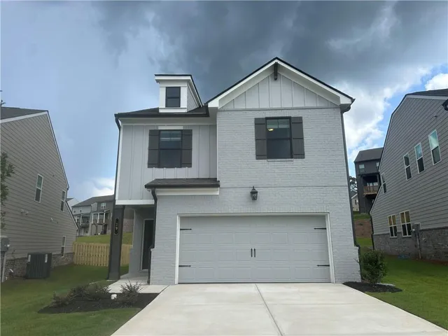Light grey painted brick facade, board and batten siding, dormer window, attached garage, and concrete driveway