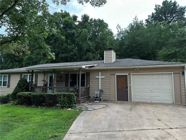 Ranch-style residence featuring a covered front porch with railings, a single-car garage, a paved driveway, and mature landscaping