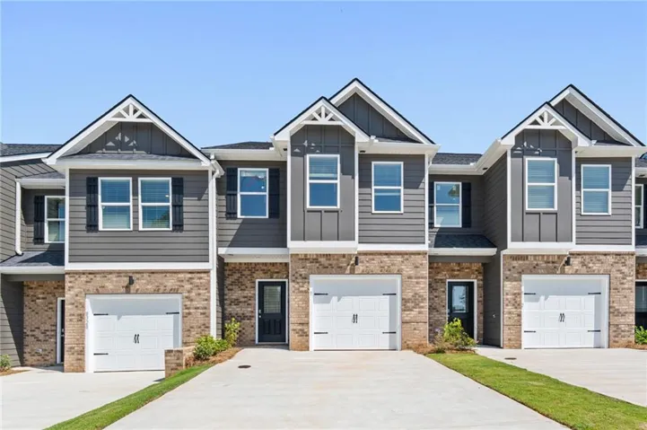 Modern townhome exterior featuring brick and siding facade, white garage doors, and individual driveways