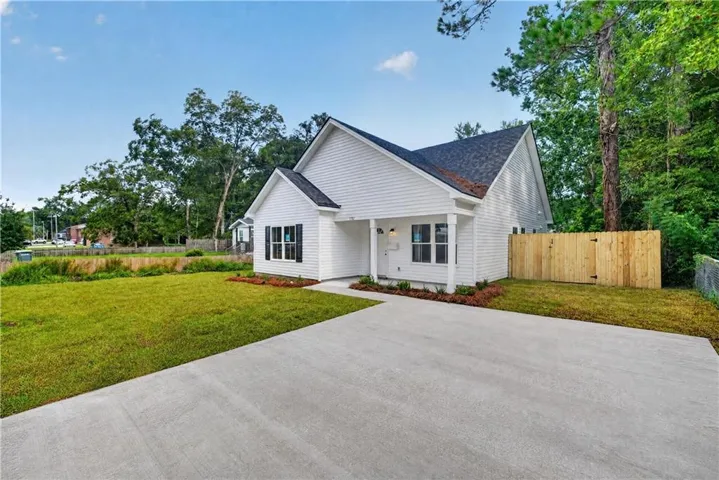 White exterior siding with dark shingle roof, expansive front lawn, concrete driveway, and wood privacy fence