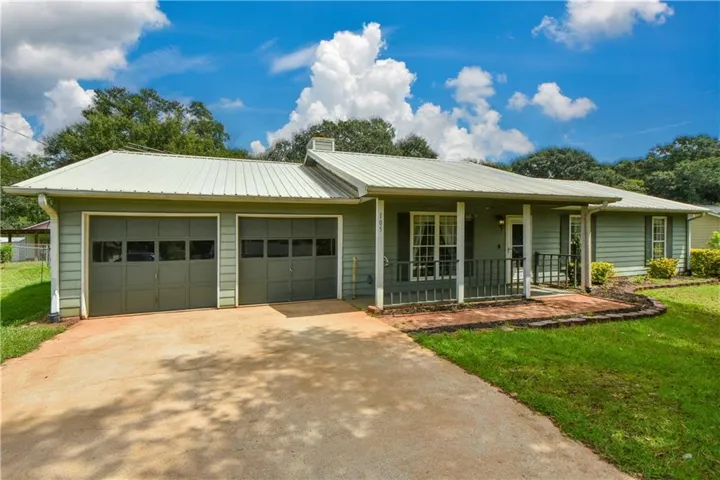 Siding exterior with a metal roof, two-car garage, and a covered front porch with a brick-edged planting bed