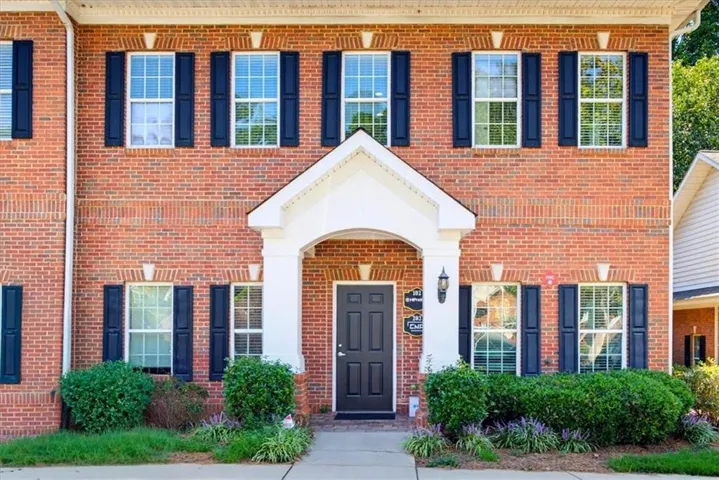 Brick exterior with dark shutters, covered entry with columns, black paneled front door, and mature landscaping