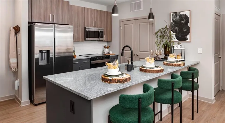 Kitchen featuring appliances with stainless steel finishes, tasteful backsplash, light wood-style floors, hanging light fixtures, and a breakfast bar
