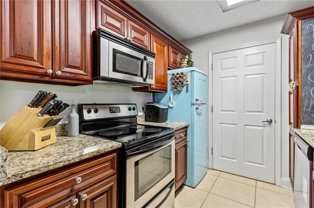 Kitchen with a textured ceiling, light stone countertops, light tile floors, and stainless steel appliances