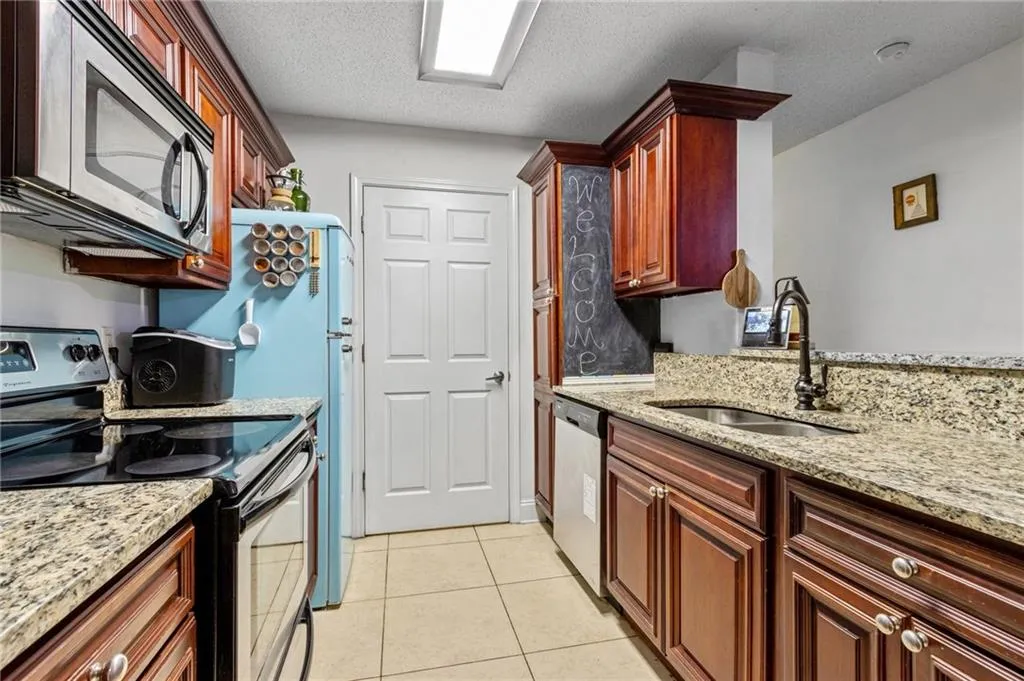 Kitchen featuring a textured ceiling, stainless steel appliances, light stone counters, sink, and light tile flooring