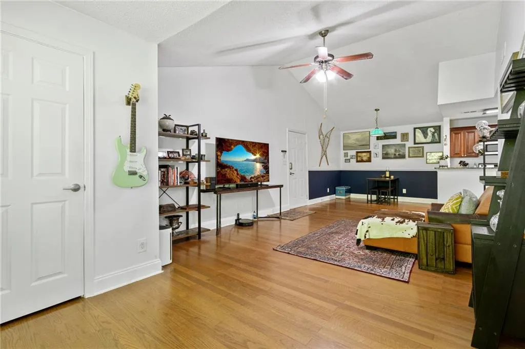Living room featuring high vaulted ceiling, a textured ceiling, ceiling fan, and light wood-type flooring