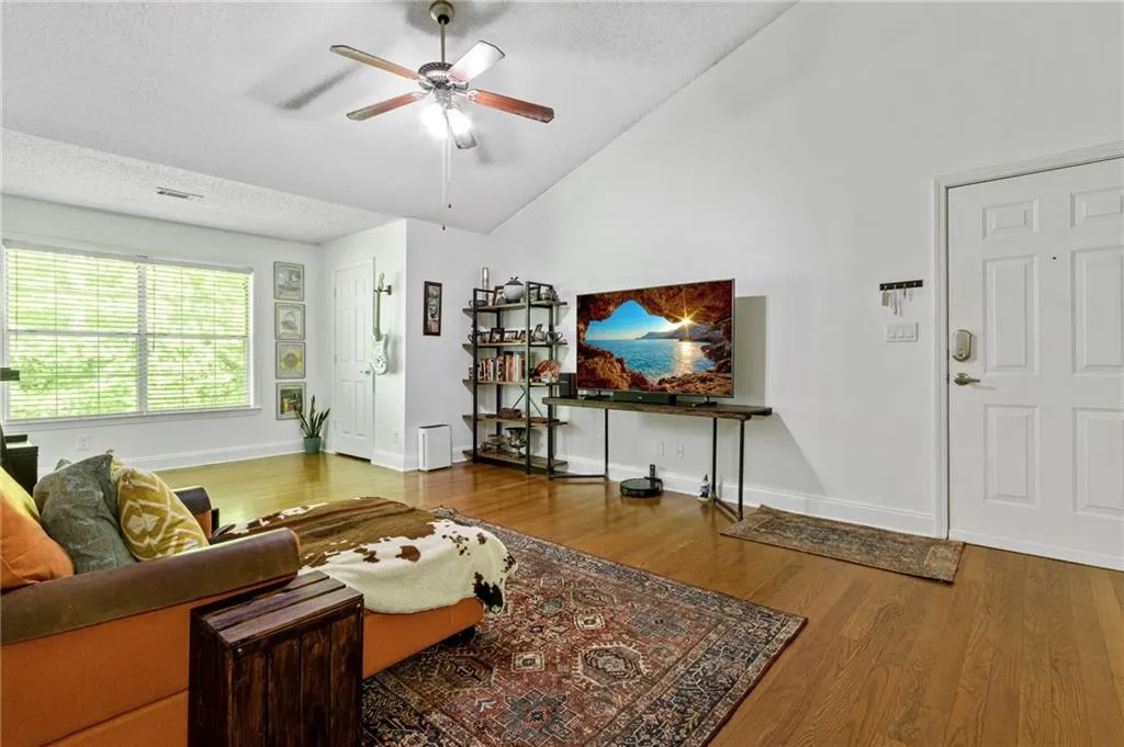 Living room featuring high vaulted ceiling, ceiling fan, a textured ceiling, and hardwood / wood-style flooring