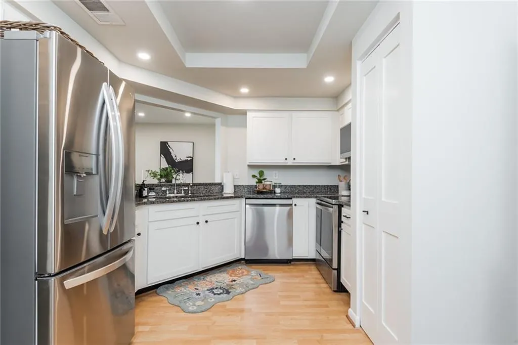 Kitchen featuring a raised ceiling, white cabinets, appliances with stainless steel finishes, and light hardwood / wood-style flooring