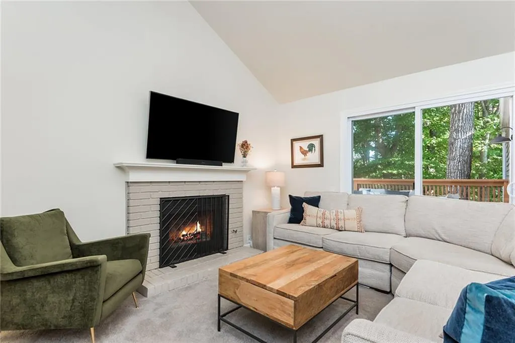 Living room with a brick fireplace, high vaulted ceiling, and light colored carpet