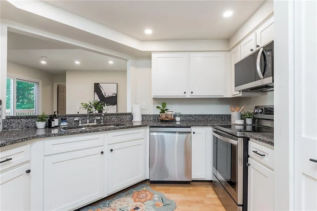 Kitchen with stainless steel appliances, white cabinets, sink, light hardwood / wood-style floors, and dark stone counters