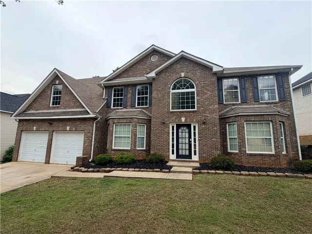 Brick exterior featuring a two-car garage, prominent arched window, bay window, and a dark paneled front door with sidelights