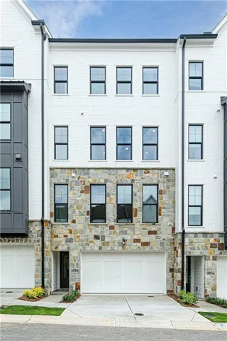 Contemporary townhome facade featuring white brick, natural stone veneer, a two-car garage, black-framed windows, and a prominent bay window with dark paneling