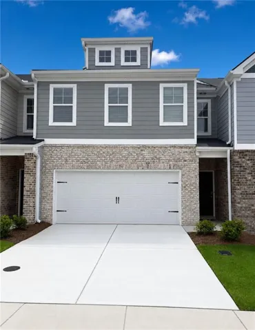 Modern townhome exterior featuring a two-car garage, light-colored brick facade, gray horizontal siding, and white-framed windows