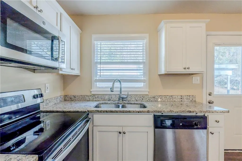 Kitchen with white cabinetry, sink, light stone counters, and stainless steel appliances