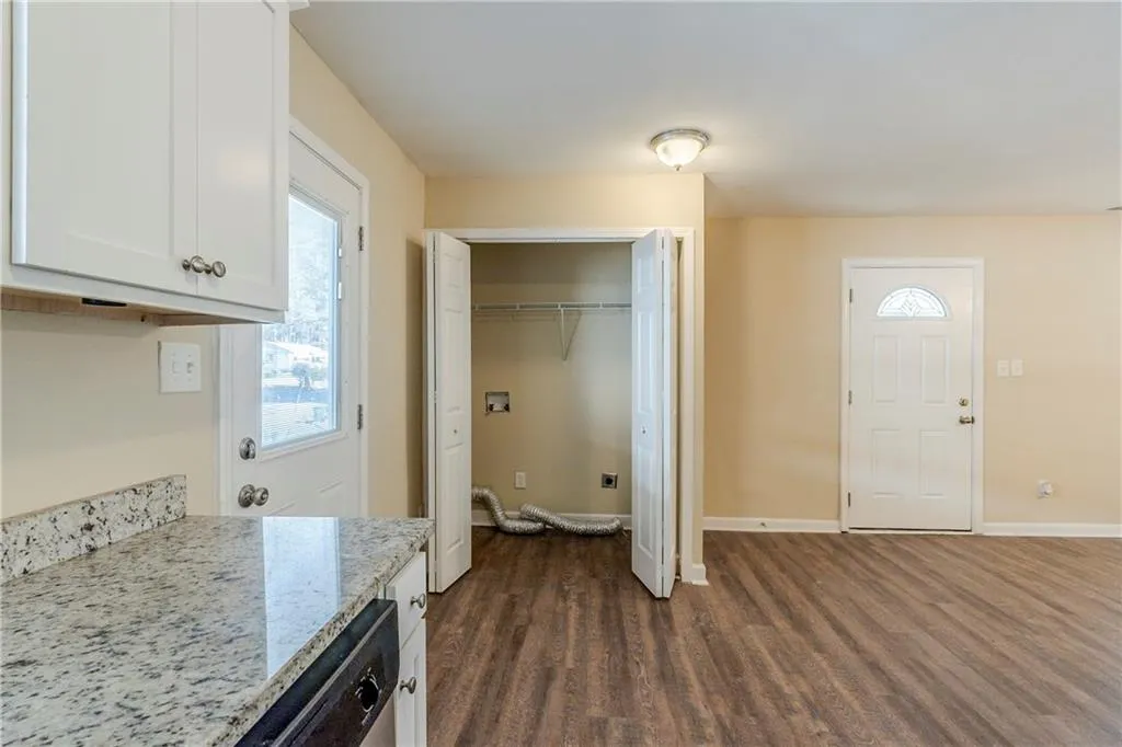 Kitchen with white cabinetry, dark wood-type flooring, light stone countertops, and dishwasher