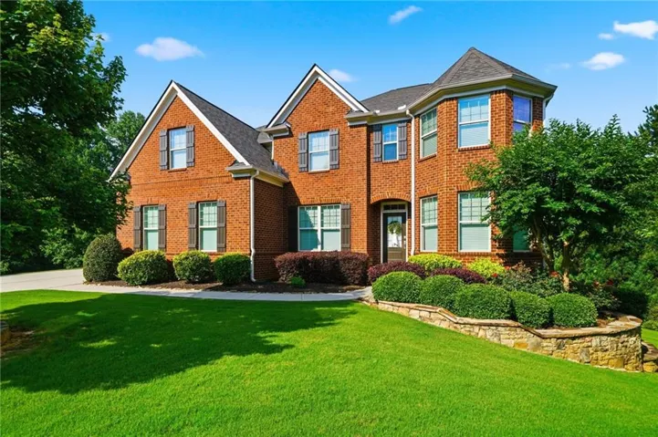 Brick Colonial estate showcasing a symmetrical façade with multiple gabled rooflines, arched entryway, and professionally landscaped grounds featuring a manicured lawn, mature foundation plantings, and stone border edging