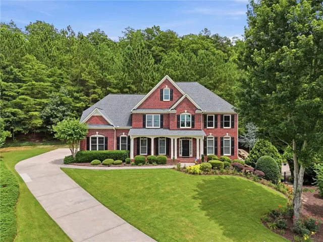 Brick exterior with a shingled roof, a curved driveway, and manicured landscaping