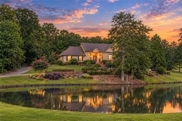 Expansive property featuring a tranquil pond, lush green landscaping, mature trees, and a paved driveway