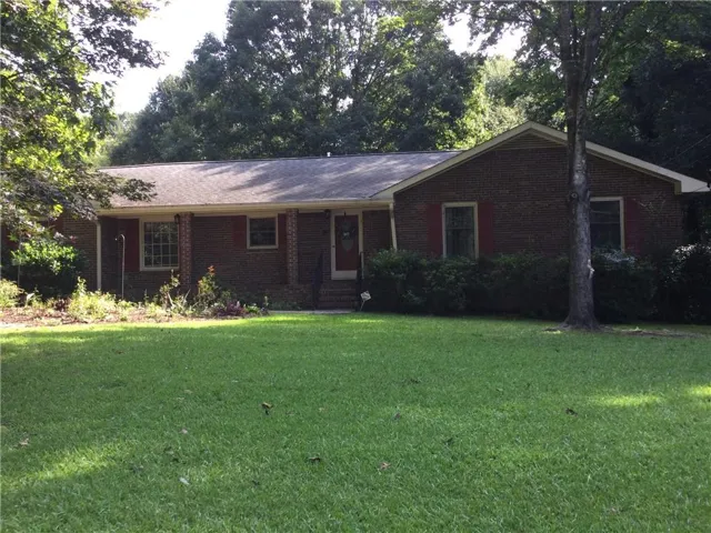 Brick exterior with an inviting covered porch, mature front yard landscaping, and an expansive lawn