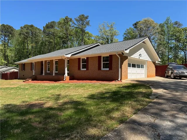 Brick ranch-style residence featuring a covered front porch with white columns, a pitched shingle roof, and an attached single-car garage with a white door