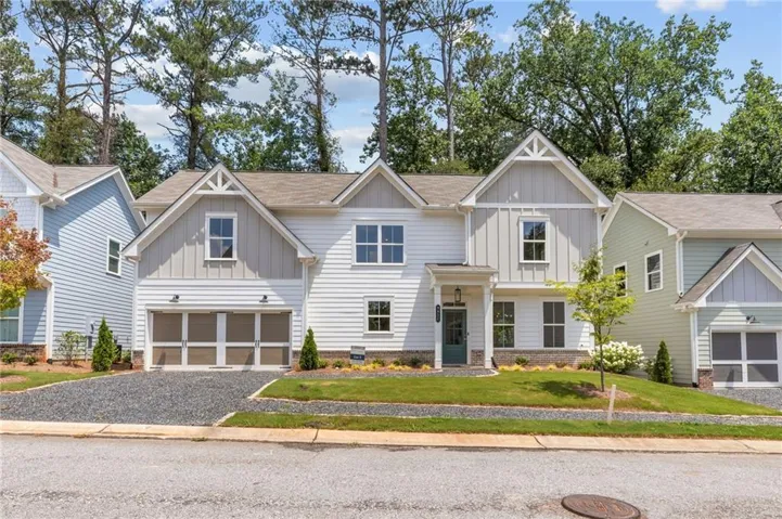 Modern farmhouse exterior featuring white siding, a covered entry, an attached two-car garage, an asphalt driveway, and a front lawn