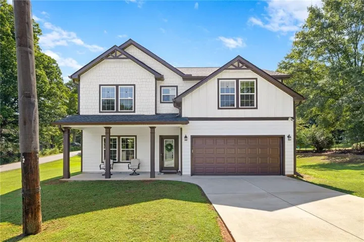 Two-story residence featuring white siding, dark trim accents, a covered front porch, a two-car garage, and a concrete driveway