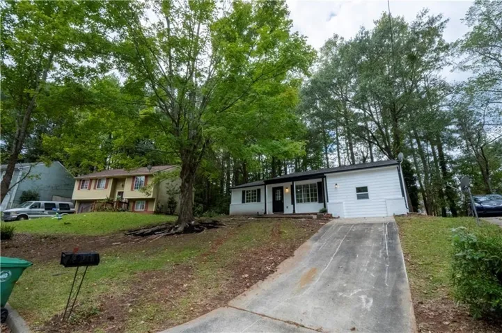 White exterior siding with dark trim accents, concrete driveway, and mature landscaping
