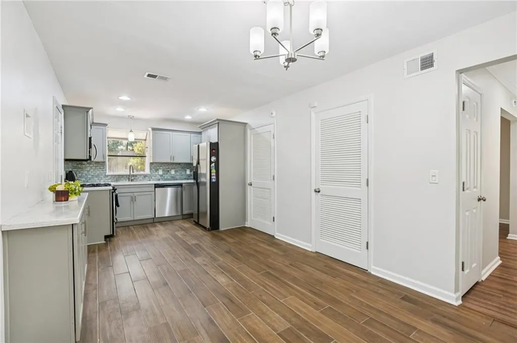 Kitchen with appliances with stainless steel finishes, gray cabinetry, dark wood finished floors, backsplash, and a chandelier
