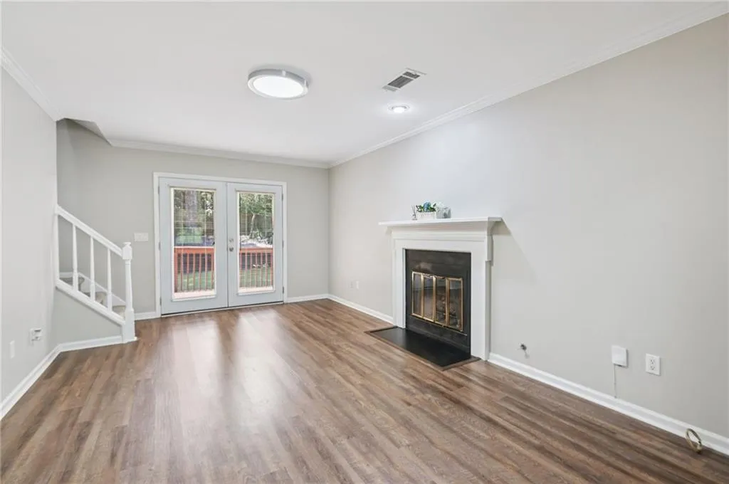 Unfurnished living room featuring stairs, wood finished floors, french doors, a glass covered fireplace, and ornamental molding