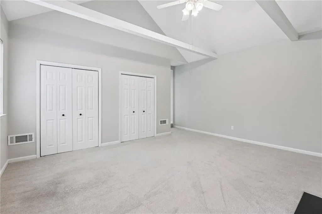 Unfurnished bedroom featuring high vaulted ceiling, carpet, multiple closets, and a ceiling fan